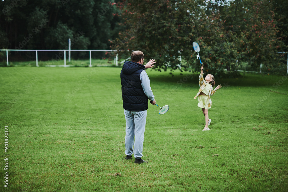 Teenage girl playing badminton with her father on green grass in summer park Teenage girl playing badminton with her father on green grass in summer park