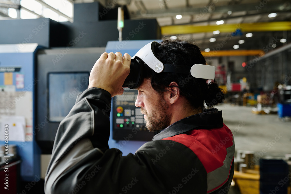 Man engaged in using a virtual reality headset in spacious industrial setting, operating advanced machinery Man engaged in using a virtual reality headset in spacious industrial setting, operating advanced machinery