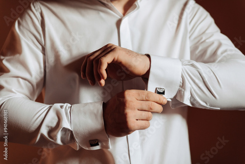 A man is getting dressed in a white shirt and is adjusting his cuff. Concept of formality and attention to detail, as the man takes care to properly adjust his cuff