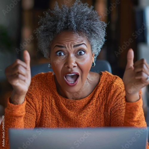 Mature older elderly black African American woman around her computer excited and happy as she focuses on the computer screen 