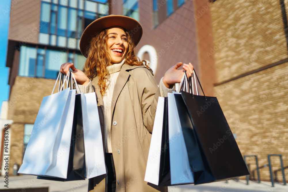 A young woman smiles brightly while holding several shopping bags in a lively urban setting, enjoying her shopping spree on a beautiful day. Consumerism, sale, purchases, shopping, lifestyle concept. A young woman smiles brightly while holding several shopping bags in a lively urban setting, enjoying her shopping spree on a beautiful day. Consumerism, sale, purchases, shopping, lifestyle concept.