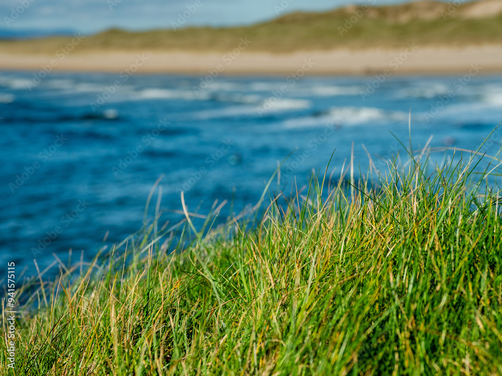 Green grass grows on cliff and amazing waves and sandy Bundoran beach in Ireland on warm sunny day. Popular tourist and surfers area. Blue cloudy sky. Irish landscape. Rich saturated color. Green grass grows on cliff and amazing waves and sandy Bundoran beach in Ireland on warm sunny day. Popular tourist and surfers area. Blue cloudy sky. Irish landscape. Rich saturated color.