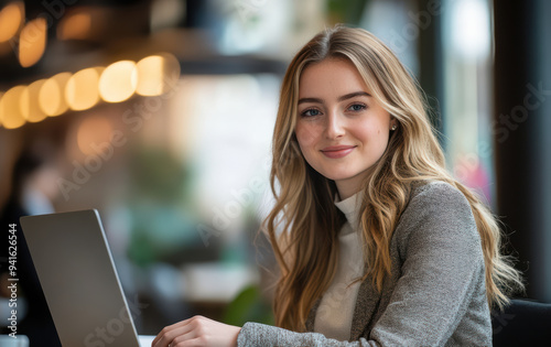 A confident businesswoman smiles while productively working on her laptop in a bright, modern office space.