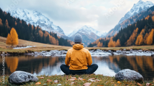 A person sits peacefully by serene lake, surrounded by majestic mountains and autumn foliage, reflecting sense of tranquility and connection with nature.