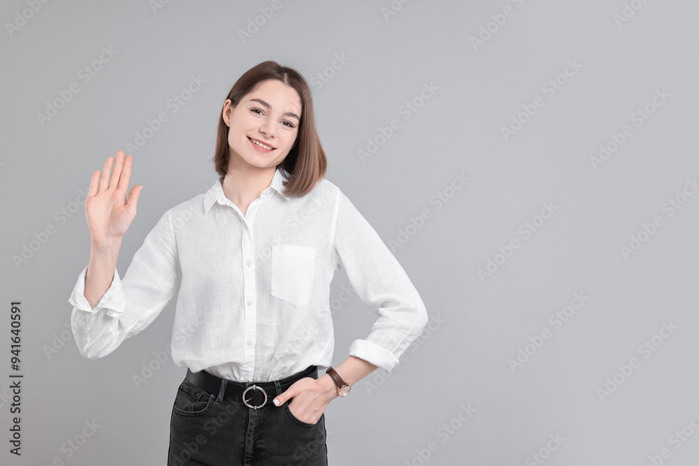Happy teenage girl waving on gray background, space for text Happy teenage girl waving on gray background, space for text