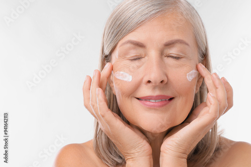 Senior woman with face cream on white background