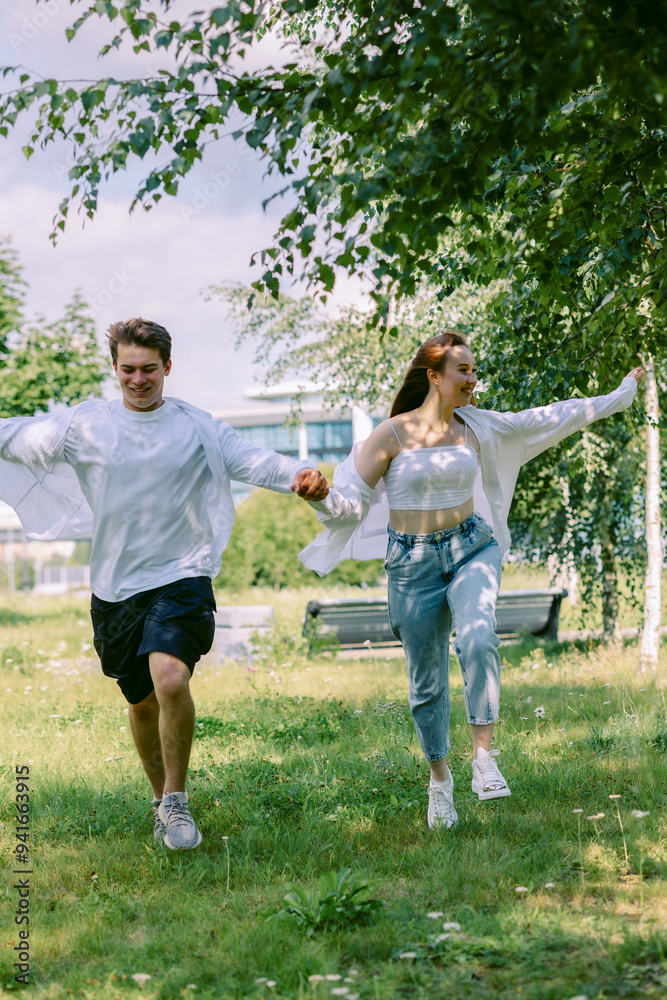Fototapeta premium Loving couple of young girl and man are walking and having fun in park on warm summer day. Vertical photo. High quality photo