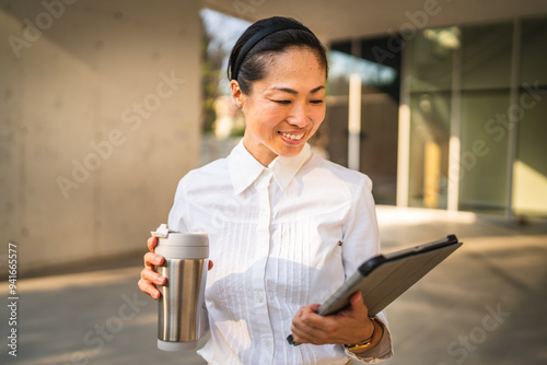 Mature japanese business woman use digital tablet and hold thermos photo