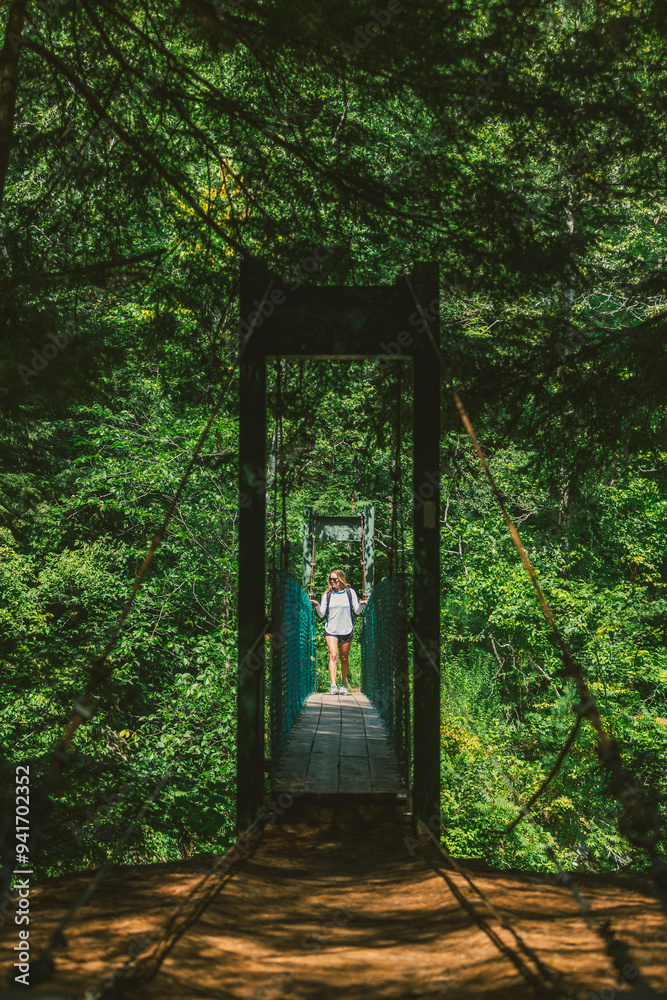Woman with long blonde hair walking on a suspension bridge above Clarendon Gorge, Vermont with backpack in the green forest in nature outdoors in summer. Woman with long blonde hair walking on a suspension bridge above Clarendon Gorge, Vermont with backpack in the green forest in nature outdoors in summer.
