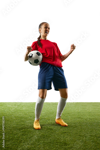 Full-length photo of young, female football athlete celebrates game-changing moment standing on stadium with ball and shouting of joy. Concept of women and sport, team games, victory, action. Ad photo