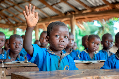 10 year old African children in blue uniforms sitting at desks in a classroom in an African rural school, one boy raises his hand to answer