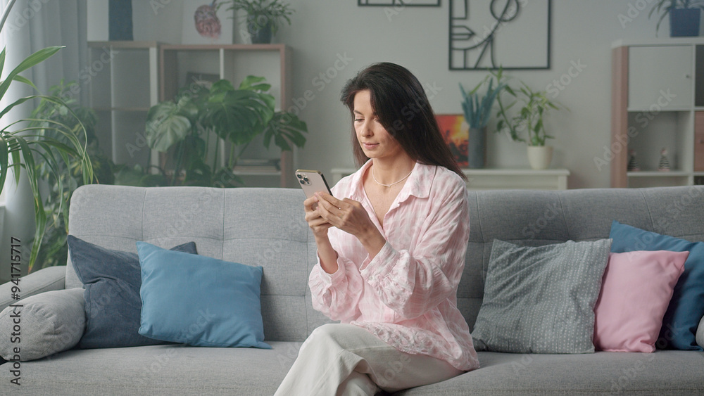 Woman using smartphone while relaxing on sofa at Woman using smartphone while relaxing on sofa at