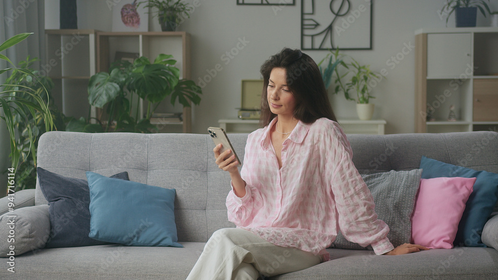 Woman using smartphone while relaxing on sofa at Woman using smartphone while relaxing on sofa at