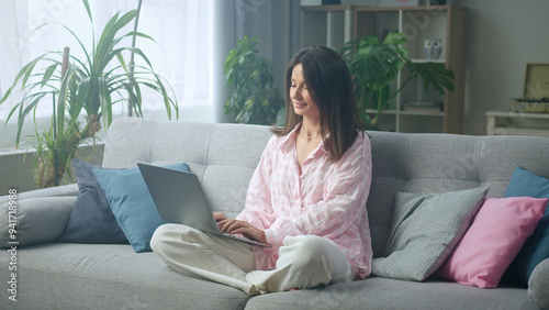 Young woman sitting on sofa using laptop in cozy