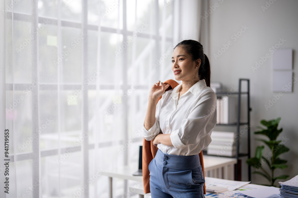 Businesswoman holding blazer looking out window in office Businesswoman holding blazer looking out window in office