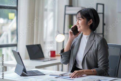 Asian businesswoman talking on the phone and working on a laptop in her office
