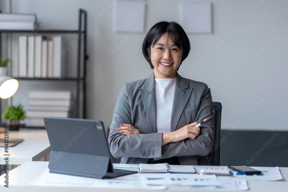 Asian businesswoman smiling at camera holding pen with arms crossed in office Asian businesswoman smiling at camera holding pen with arms crossed in office