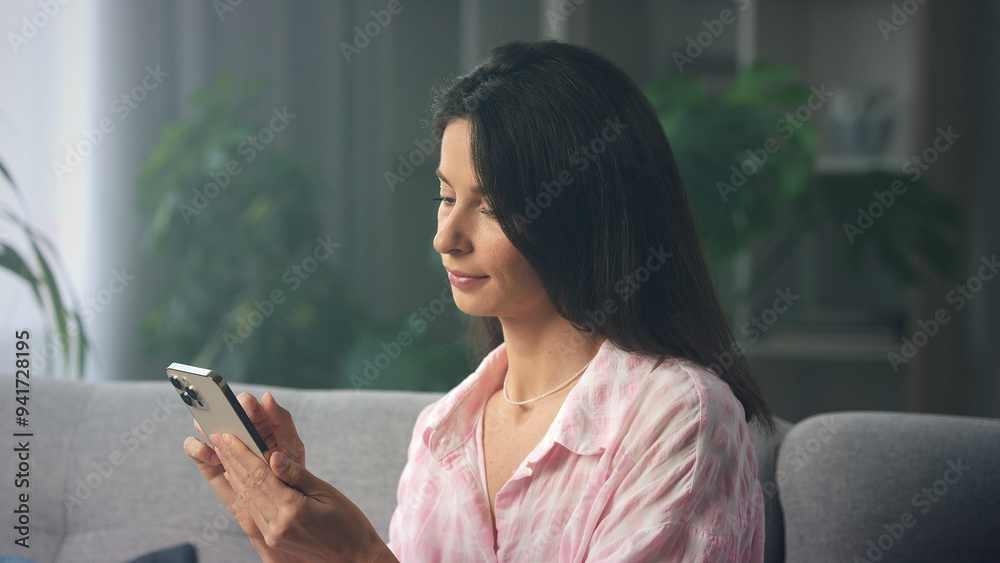 Smiling woman using smartphone at home on sofa