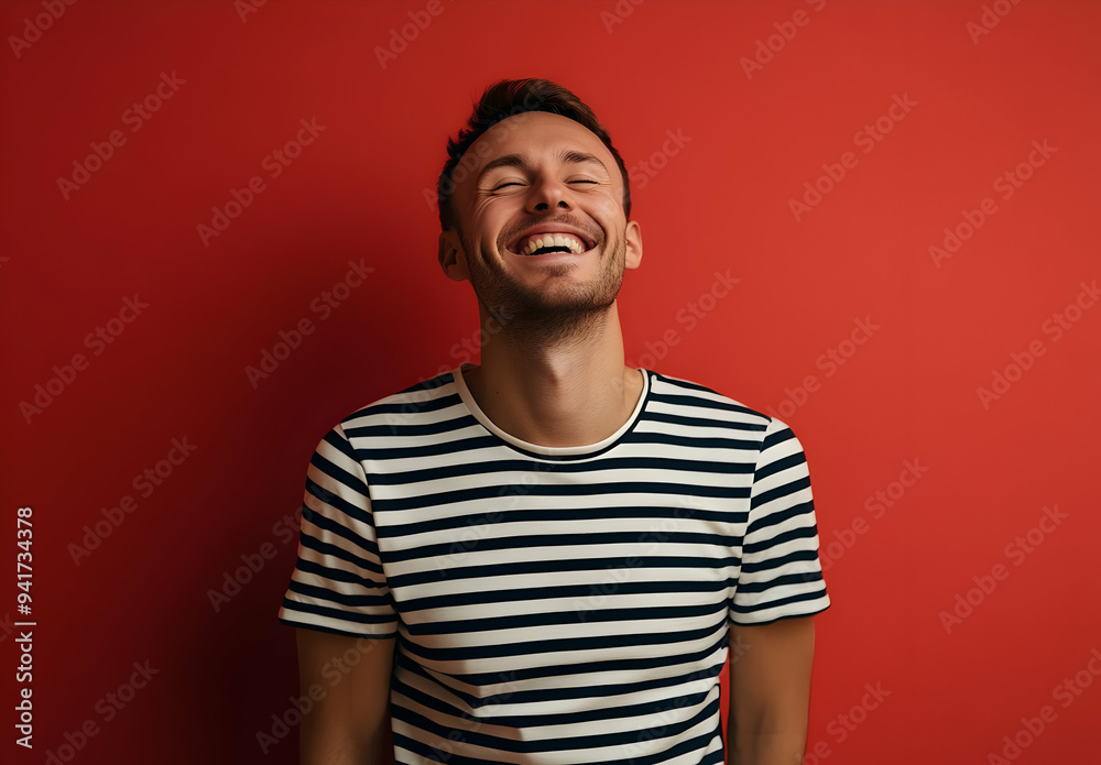 A cheerful man in a striped shirt smiles broadly against a vibrant red background, radiating joy and positivity. A cheerful man in a striped shirt smiles broadly against a vibrant red background, radiating joy and positivity.