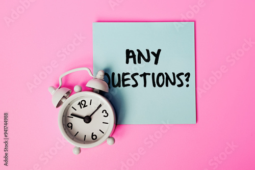 Sticky Note with 'Any Questions?' Written on It, Concept for Q&A Sessions, Inquiries, Customer Support, or Classroom Discussions. White alarm clock and Blue Note on a Pink Background