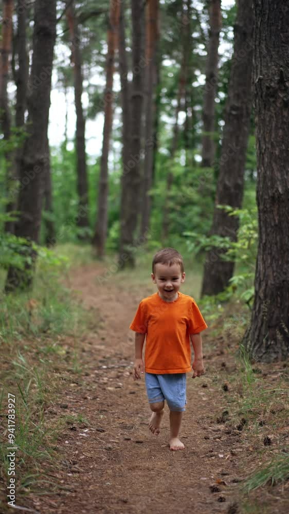 Happy smiling boy approaches camera running by the narrow path. Child walking barefoot in the forest. Vertical video. Happy smiling boy approaches camera running by the narrow path. Child walking barefoot in the forest. Vertical video.