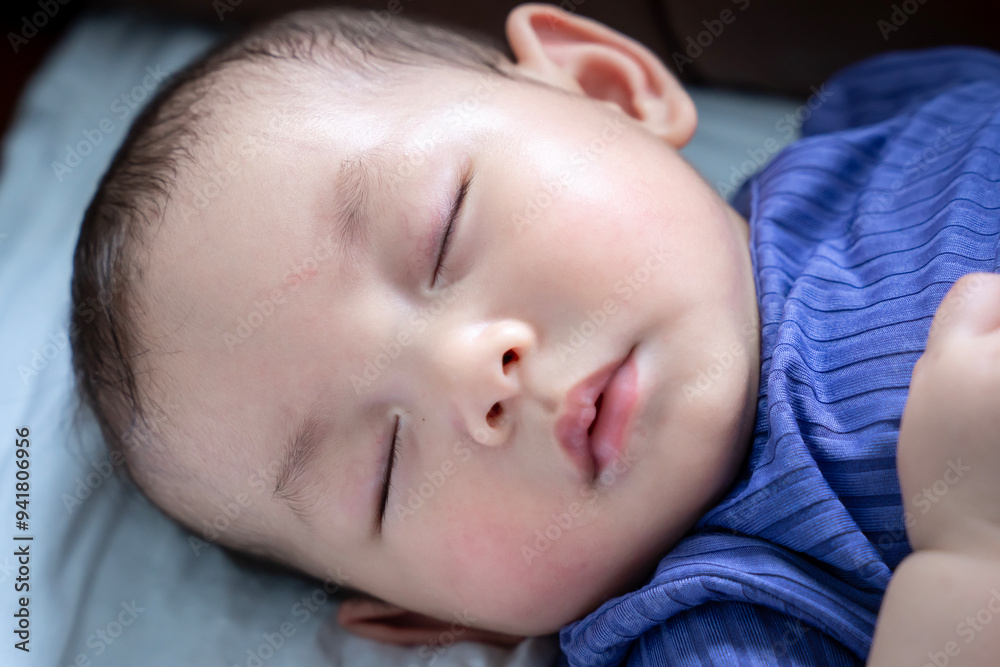 A baby is sleeping on a couch. The baby is wearing a blue outfit A baby is sleeping on a couch. The baby is wearing a blue outfit