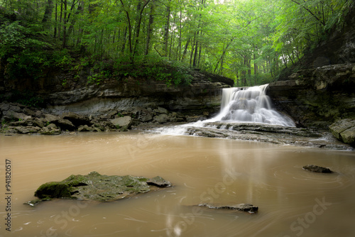 Waterfall surrounded by green forest in the summer. Muddy water. Rainy day. Green and brown. Long Expsoure. State Park. Indiana. Landscape photo