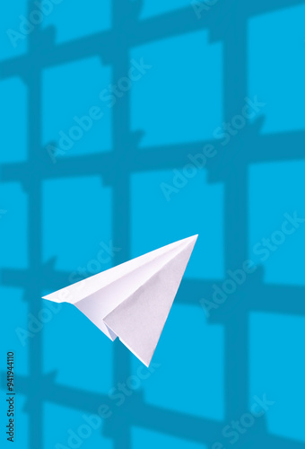 A white paper airplane flies on a blue background, the shadow of the prison bars photo