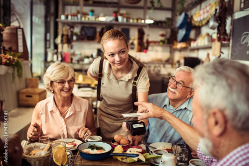 Senior man paying with smartphone for meal with friends at a restaurant