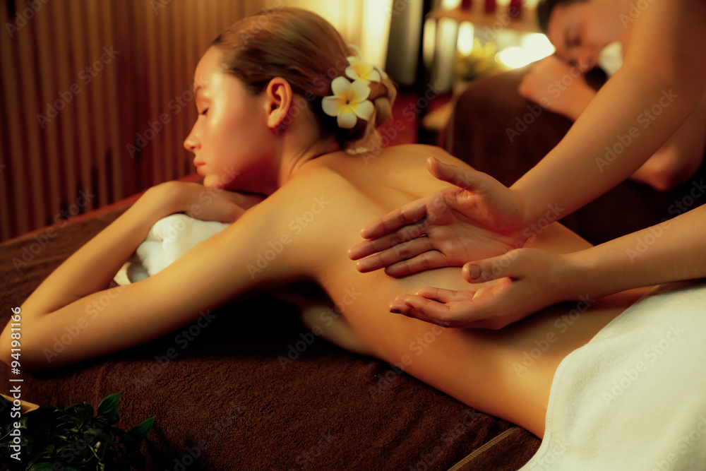 Fototapeta premium Caucasian couple customer enjoying relaxing anti-stress spa massage and pampering with beauty skin recreation leisure in warm candle lighting ambient salon spa at luxury resort or hotel. Quiescent