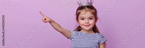 A charming young girl, approximately 6-7 years old, is wearing a crown and pointing to the side. She has a sweet, innocent expression on her face, making this image ideal for promoting children's prod