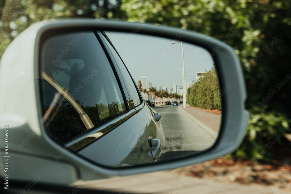 Car side mirror reflection showing a scenic road view with green surroundings in a suburban area in the background Car side mirror reflection showing a scenic road view with green surroundings in a suburban area in the background