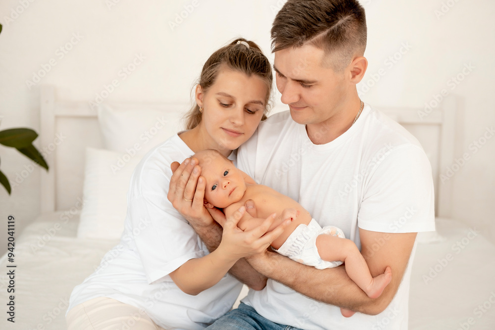 young parents with a newborn baby hug and kiss, happy mom and dad admiring the baby at home on the bed, a happy family caring for a small child, a place for text young parents with a newborn baby hug and kiss, happy mom and dad admiring the baby at home on the bed, a happy family caring for a small child, a place for text