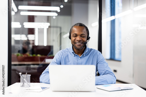 Obraz na płótnie Confident businessman wearing headset engaged in online conversation on laptop. Smiling and communicating during virtual meeting in modern office setting. Concepts of technology, work, communication w salonie