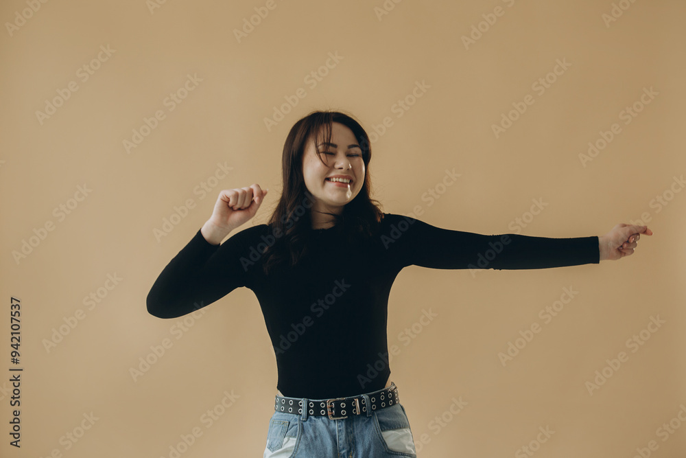 A young Asian woman is dancing on a beige background. A young Asian woman is dancing on a beige background.