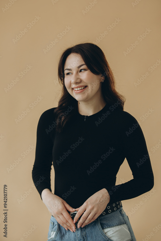 Obraz premium Beautiful cheerful cute Asian young woman looking to the side while posing isolated on beige studio background.