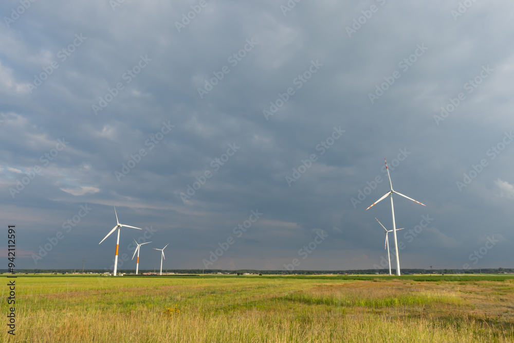 Distant white wind turbines against a dramatic cloudy sky. Meadow in the foreground, taken late afternoon