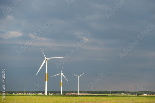 Obraz na płótnie Distant white wind turbines against a dramatic cloudy sky. Meadow in the foreground, taken late afternoon w salonie