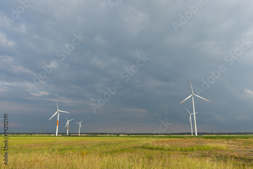 Obraz na płótnie Distant white wind turbines against a dramatic cloudy sky. Meadow in the foreground, taken late afternoon w salonie