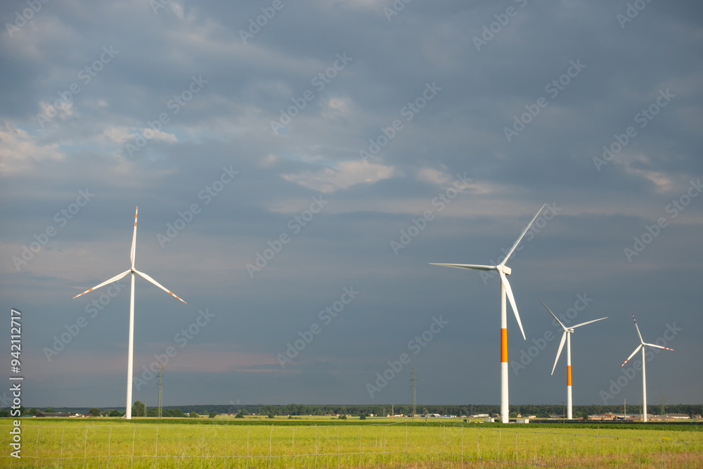 Distant white wind turbines against a dramatic cloudy sky. Meadow in the foreground, taken late afternoon
