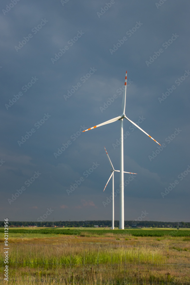 Distant white wind turbines against a dramatic cloudy sky. Meadow in the foreground, taken late afternoon
