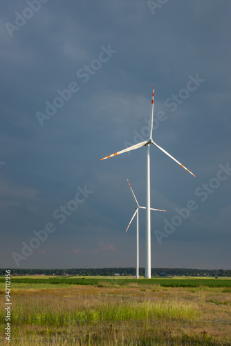 Obraz na płótnie Distant white wind turbines against a dramatic cloudy sky. Meadow in the foreground, taken late afternoon w salonie