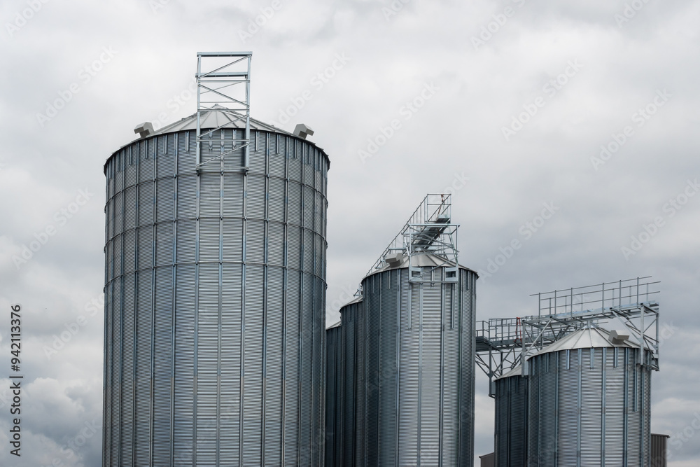 Steel grain silo against a dramatic, cloudy sky. Modern agriculture buildings photographed in the day . Steel grain silo against a dramatic, cloudy sky. Modern agriculture buildings photographed in the day .