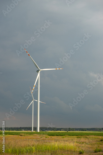 Obraz na płótnie Distant white wind turbines against a dramatic cloudy sky. Meadow in the foreground, taken late afternoon w salonie