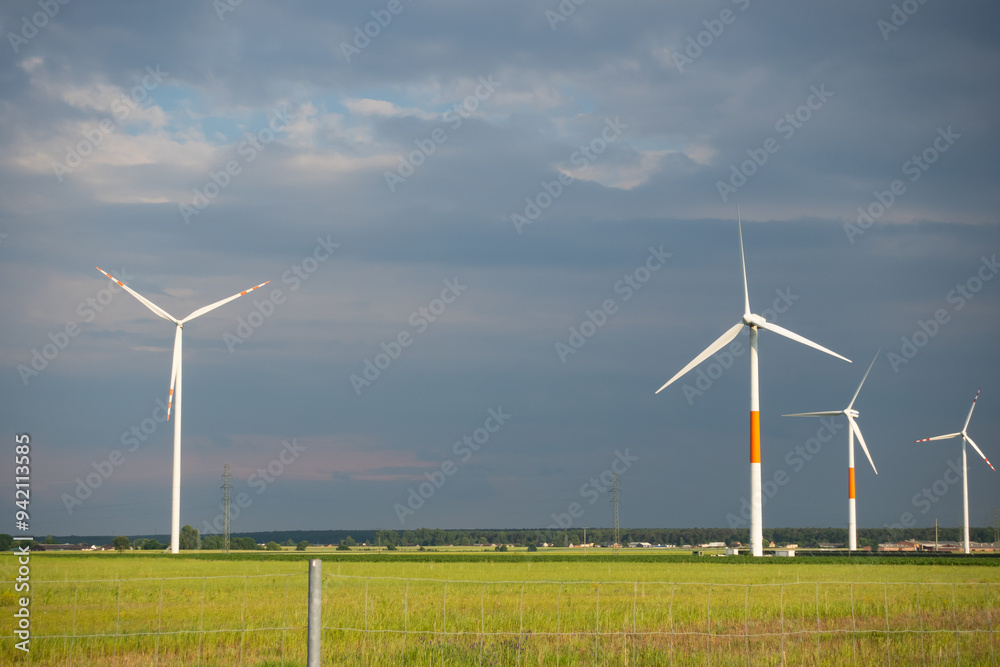 Distant white wind turbines against a dramatic cloudy sky. Meadow in the foreground, taken late afternoon