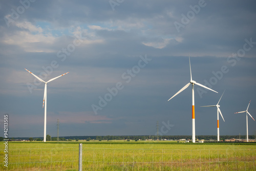 Obraz na płótnie Distant white wind turbines against a dramatic cloudy sky. Meadow in the foreground, taken late afternoon w salonie