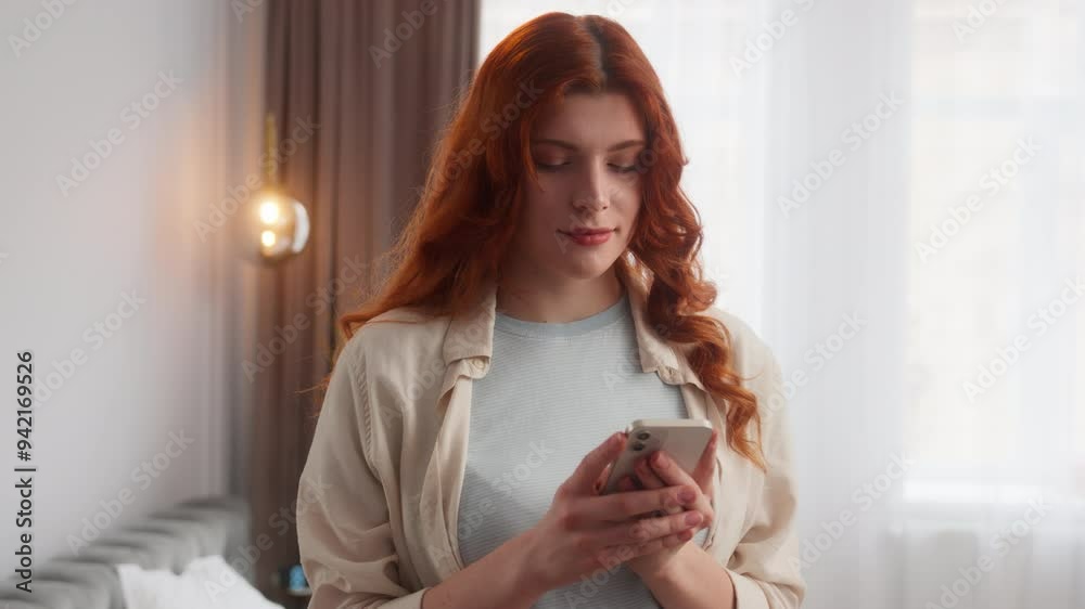 Glad Caucasian female happy woman hold smartphone read message email online in mobile phone at home. Positive girl demonstrating OK gesture in camera model smile wink recommend okay sign fine emotion