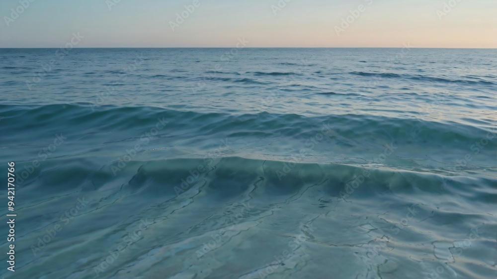 Obraz premium Soft waves rhythmically lap against the shoreline, reflecting a tranquil gradient sky as the sun sets, creating a peaceful coastal atmosphere