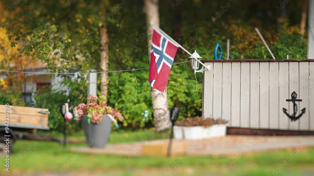 A tidy terrace in the campsite decorated with flowers, nautical symbols, and a Norwegian flag. A trailer is in the background.