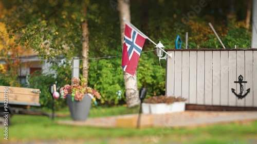 A tidy terrace in the campsite decorated with flowers, nautical symbols, and a Norwegian flag. A trailer is in the background. photo